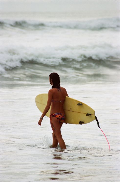 Mujer adentrandose en las aguas de santa Teresa lista para surfear